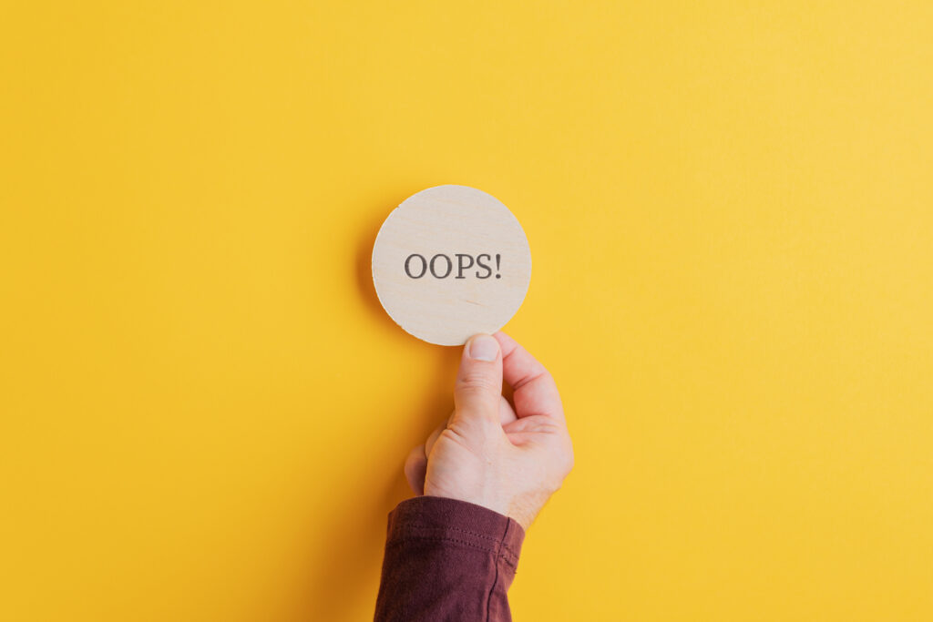 Male hand placing wooden cut circle with an Oops sign on it on bright yellow background.