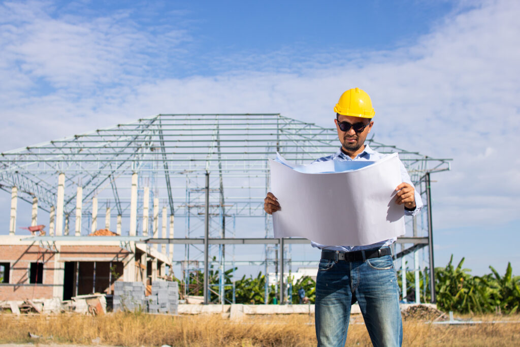 portrait of a male engineer in safety helmet and reflective vest works and check building construction blueprint plan at a working site